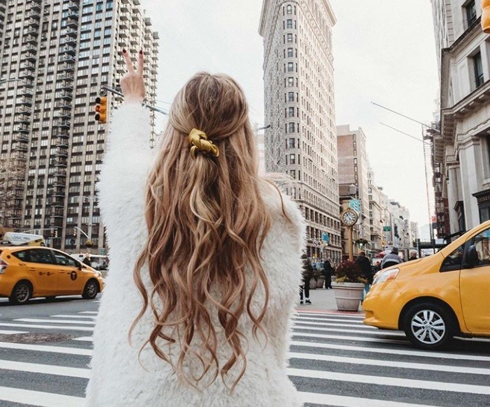 close up shot of woman with textured half up half down hairstyle, wearing white jumper and posing on the street