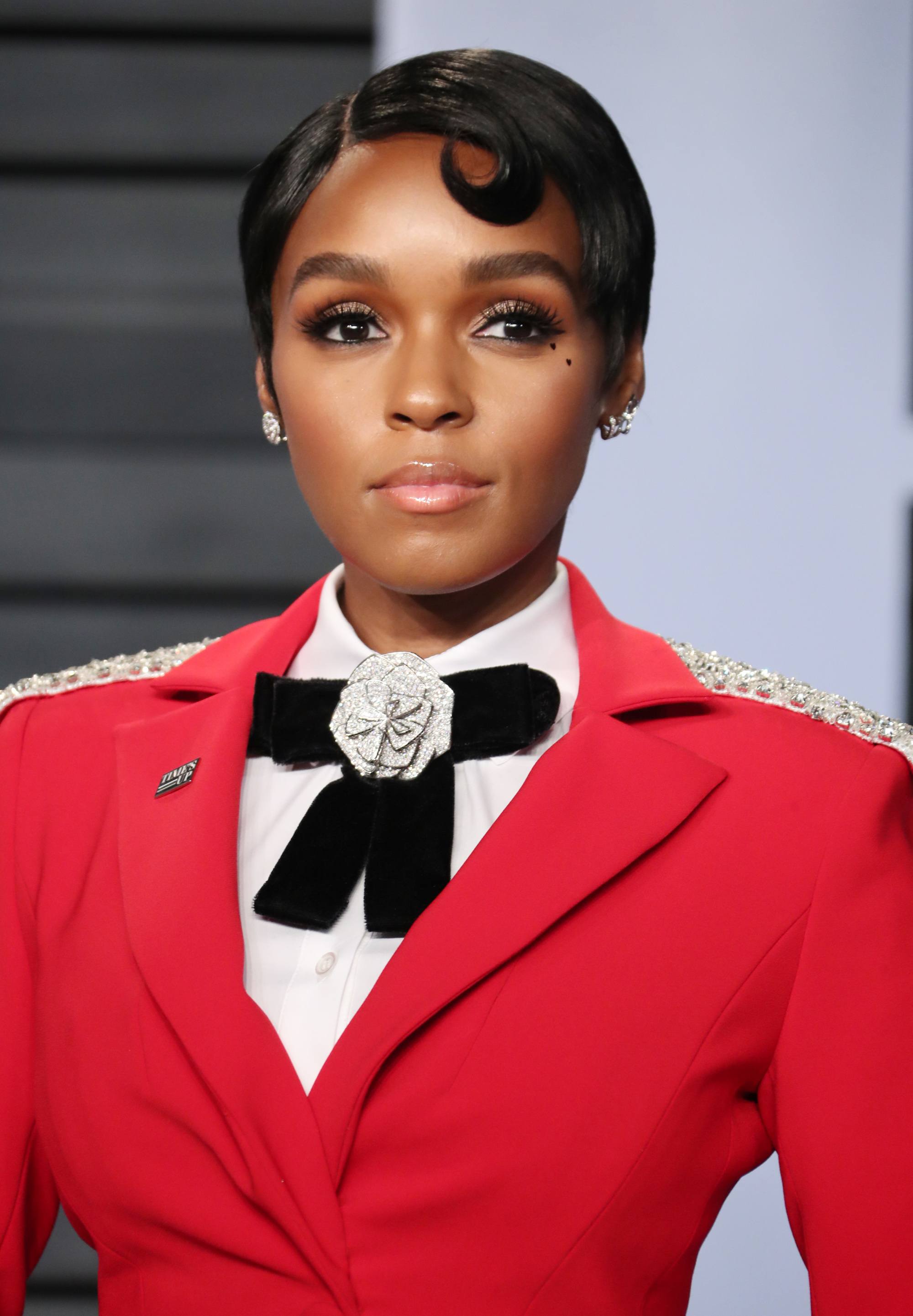 janelle monae with short dark brown pixie hair with retro wave finish wearing red blazer, white shirt and black big bow tie
