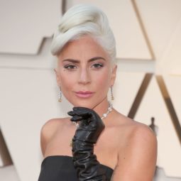 Oscars 2019 hairstyles: Lady Gaga at the 2019 Oscars with her platinum blonde hair in an Audrey Hepburn inspired chignon updo, wearing a black strapless dress and long black gloves