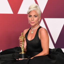 International Women's Day hair icons: Lady Gaga with a retro styled curly updo, wearing all black while holding an award