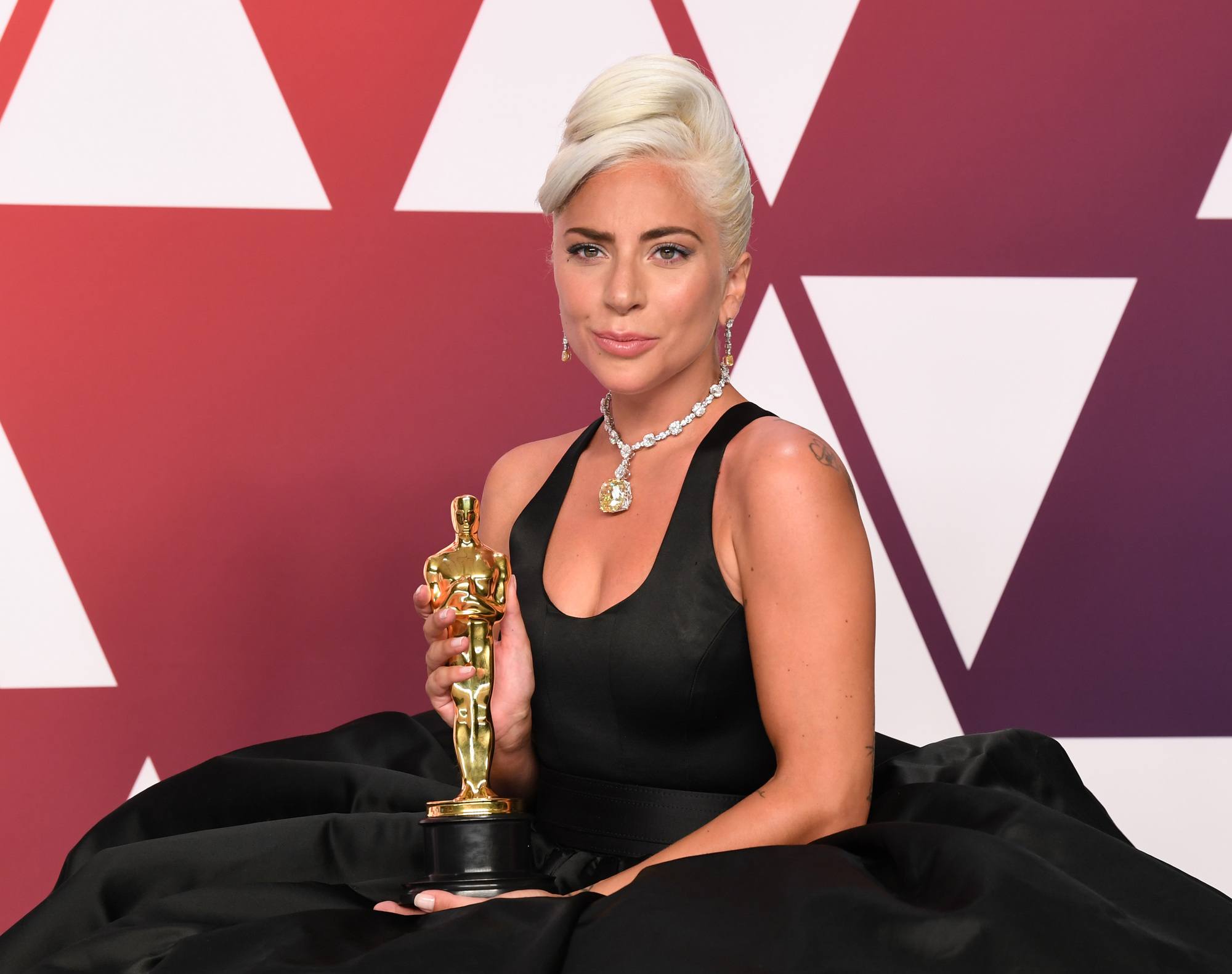International Women's Day hair icons: Lady Gaga with a retro styled curly updo, wearing all black while holding an award