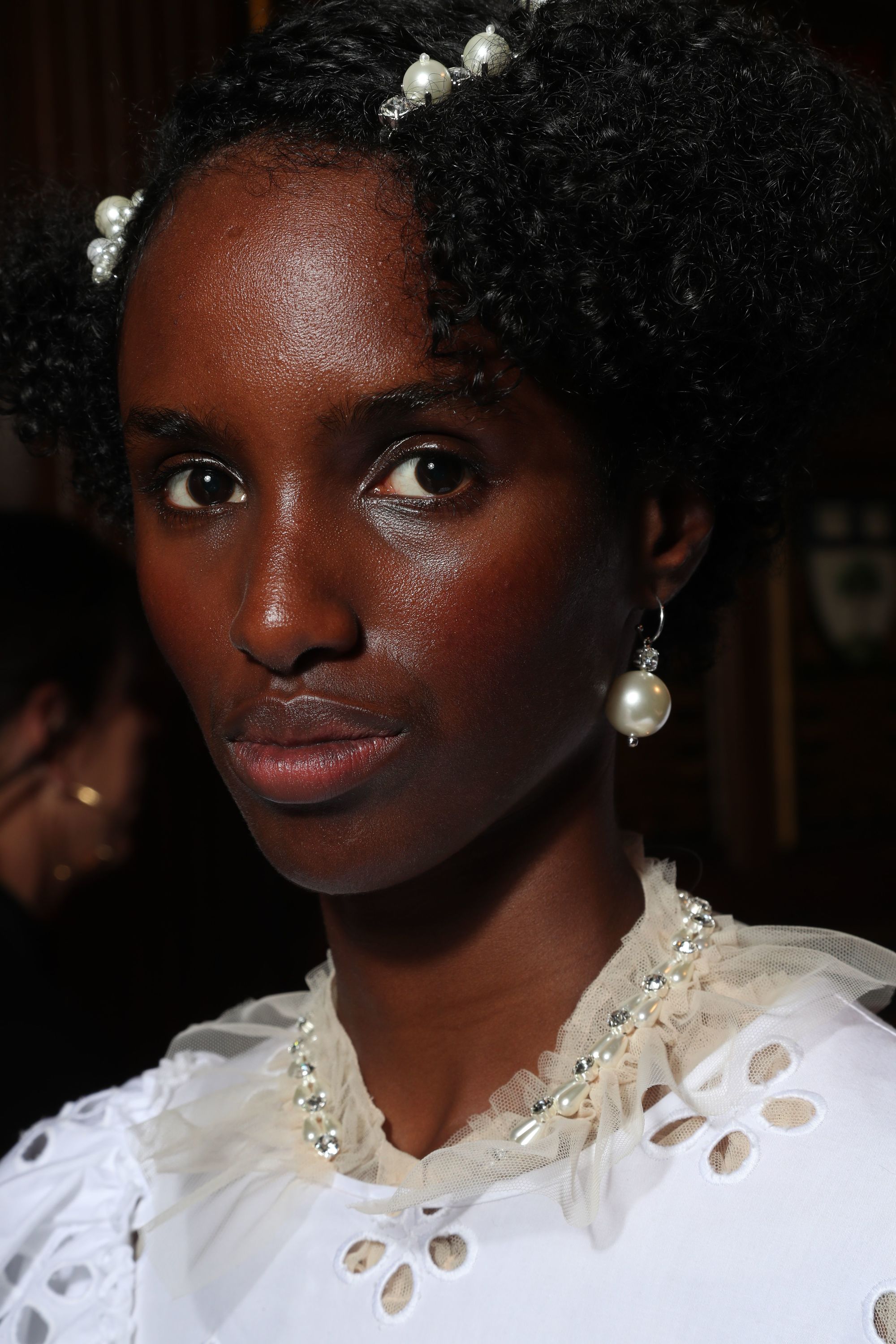 close up shot of model with natural hair with pearl hair slides in it, wearing white lace and posing backstage