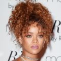 rihanna with copper brown curly hair with bangs in a pineapple updo wearing a pink bardot dress