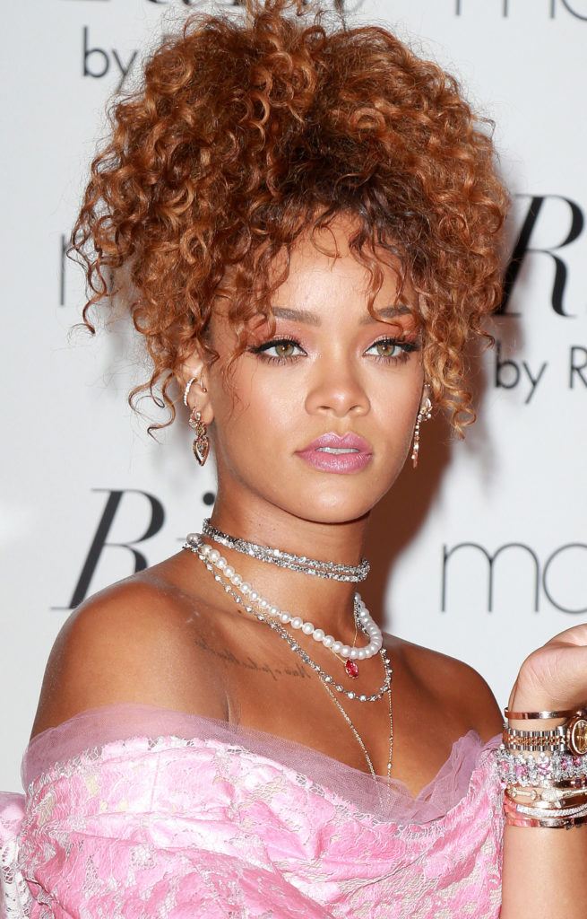 rihanna with copper brown curly hair with bangs in a pineapple updo wearing a pink bardot dress