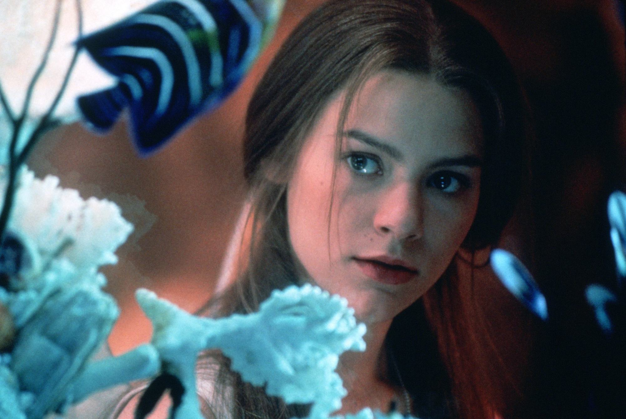 close up shot of claire danes with half-up, half-down hairstyle. wearing all white and staring at fish bowl on the set of romeo and juliet