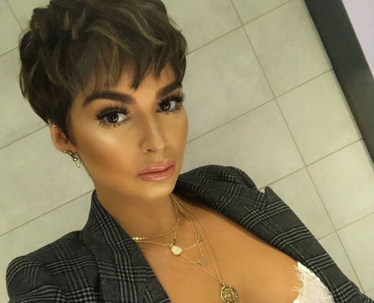 close up shot of woman with textured short pixie hairstyle, wearing checked blazer jacket and posing in a bathroom