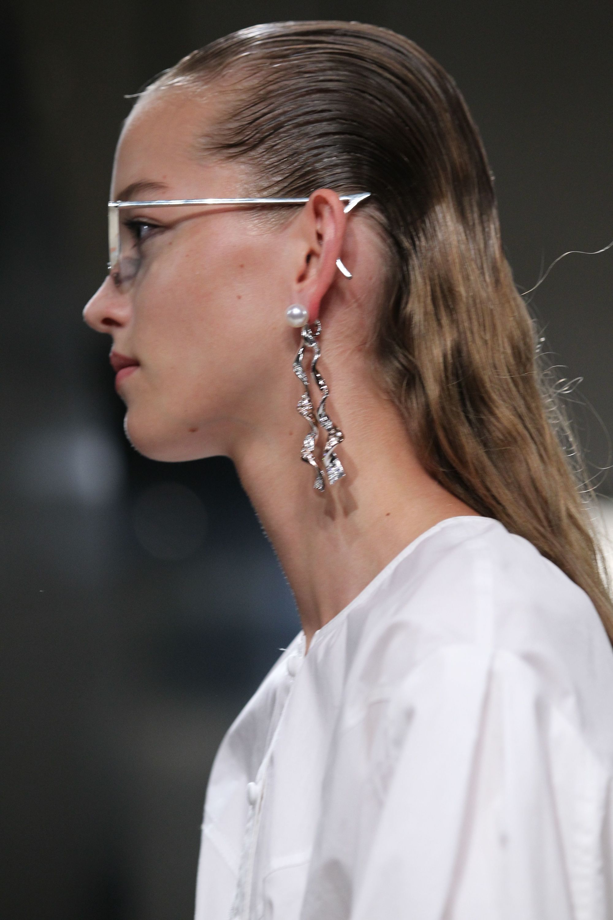 side view of model on runway with long blonde slick back wet look hair wearing sunglasses and white dress