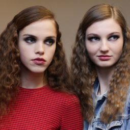 models backstage with medium length hair in side parting with smooth roots and wavy lengths wearing red jumper and denim jacket