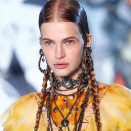 Paris Fashion Week SS19: Close up shot of a model on the Alexander Mcqueen runway with long, dark brown sleek pigtails, wearing yellow jacket with tonnes of jewellery