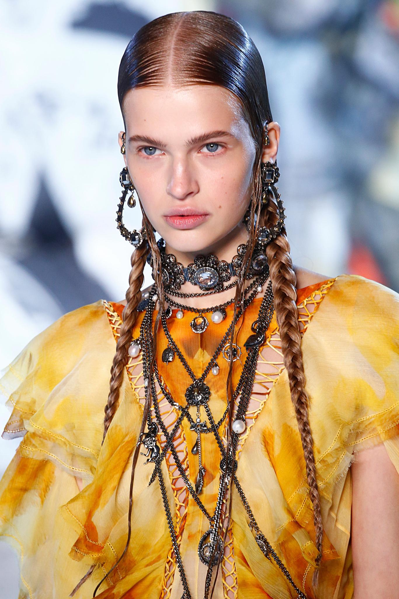 Paris Fashion Week SS19: Close up shot of a model on the Alexander Mcqueen runway with long, dark brown sleek pigtails, wearing yellow jacket with tonnes of jewellery