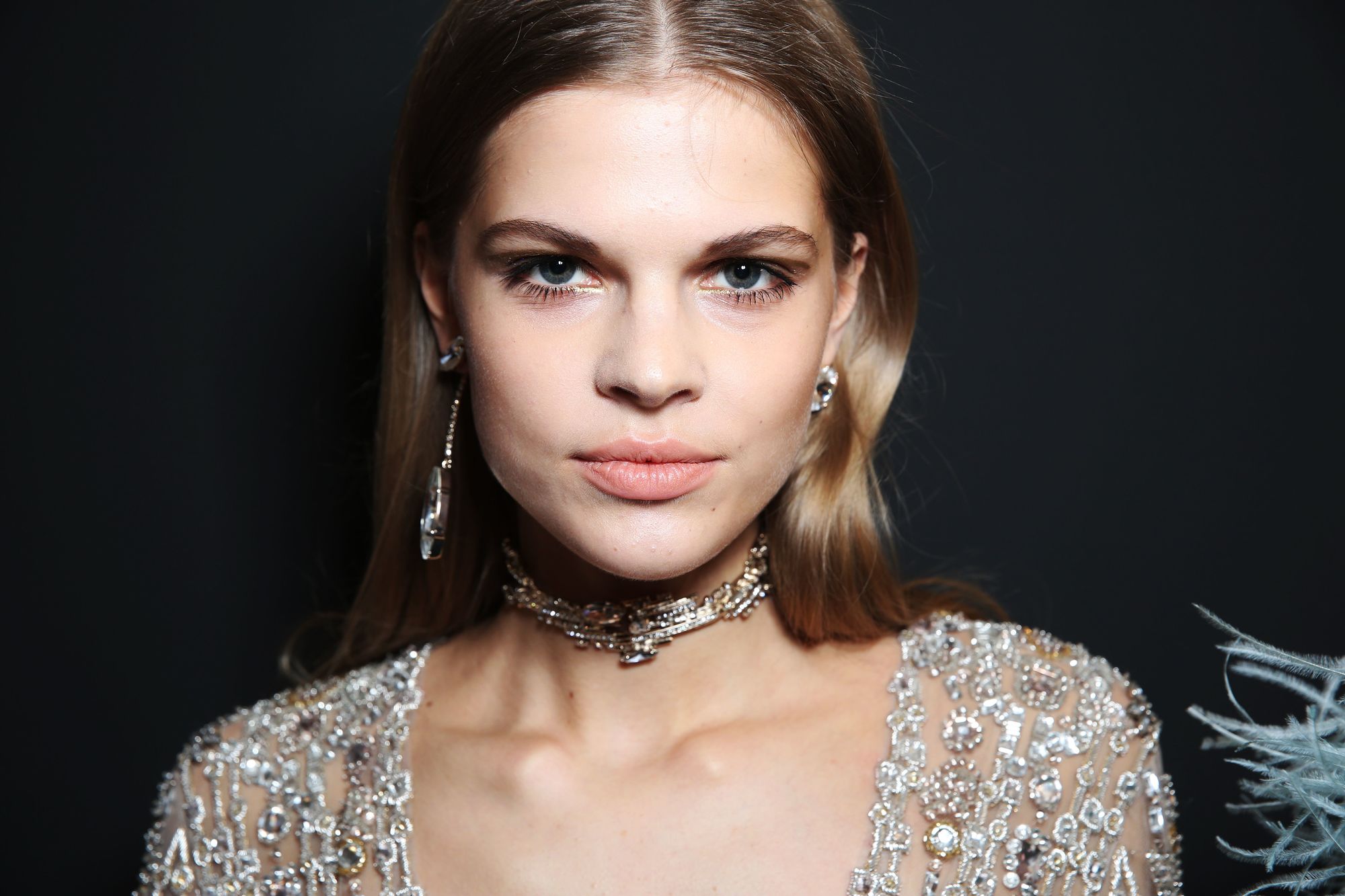 prom hairstyles: close up shot of model with polished waves hair, wearing glittery gown and neck choker, backstage at a show