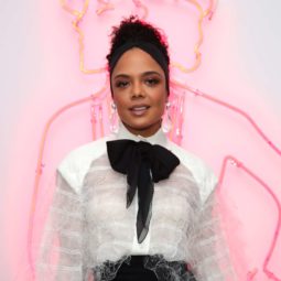 tessa thompson with dark brown hair in updo with thick black headband wearing a white shirt and big bow tie