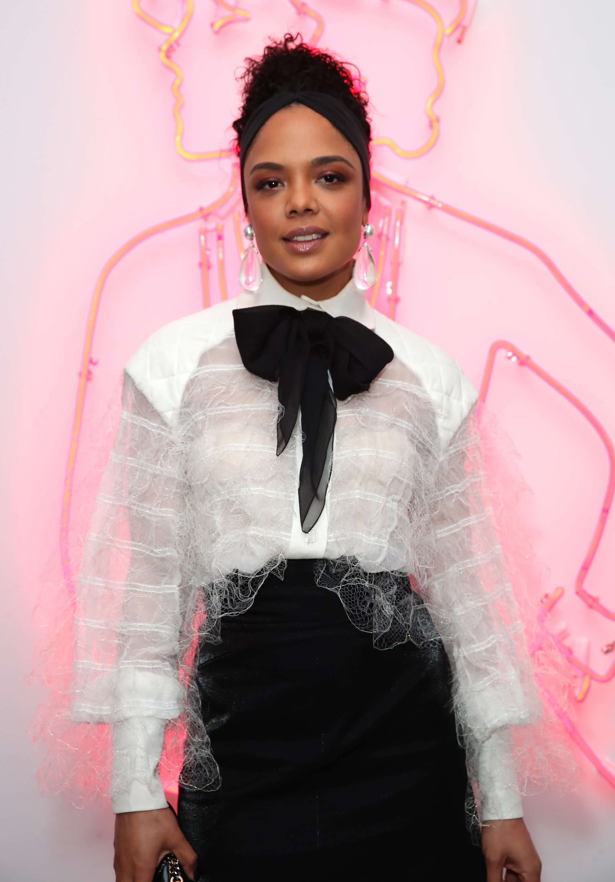 tessa thompson dark brown hair in updo with thick black headband wearing white shirt and big bow tie