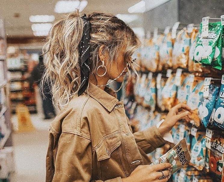 textured hairstyles: close up Instagram shot of woman in a shop, with a messy high ponytail and hair scarf, wearing all tan and sunglasses