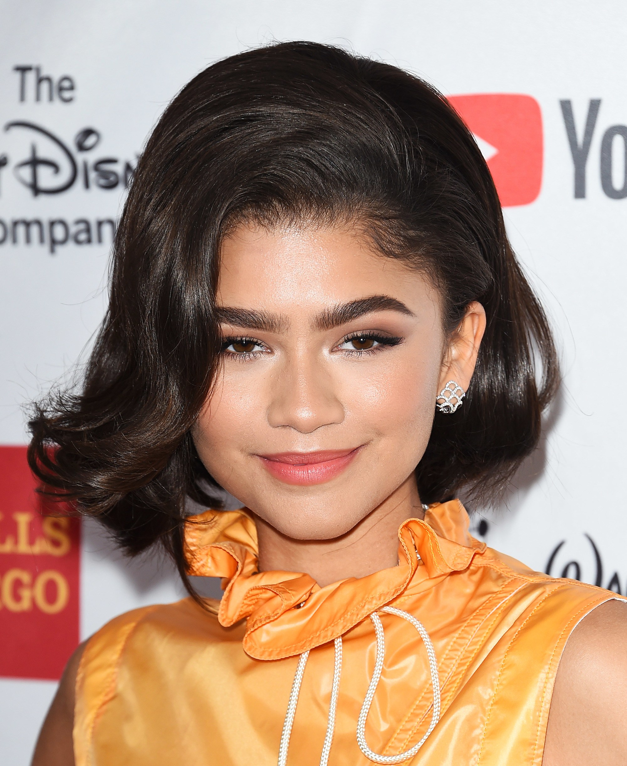 zendaya with brown '60s-inspired voluminous short hairstyle with curled ends wearing yellow high neck top