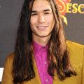 twilight actor booboo stewart on the red carpet with his long wavy dark hair wearing a pink shirt and mustard blazer