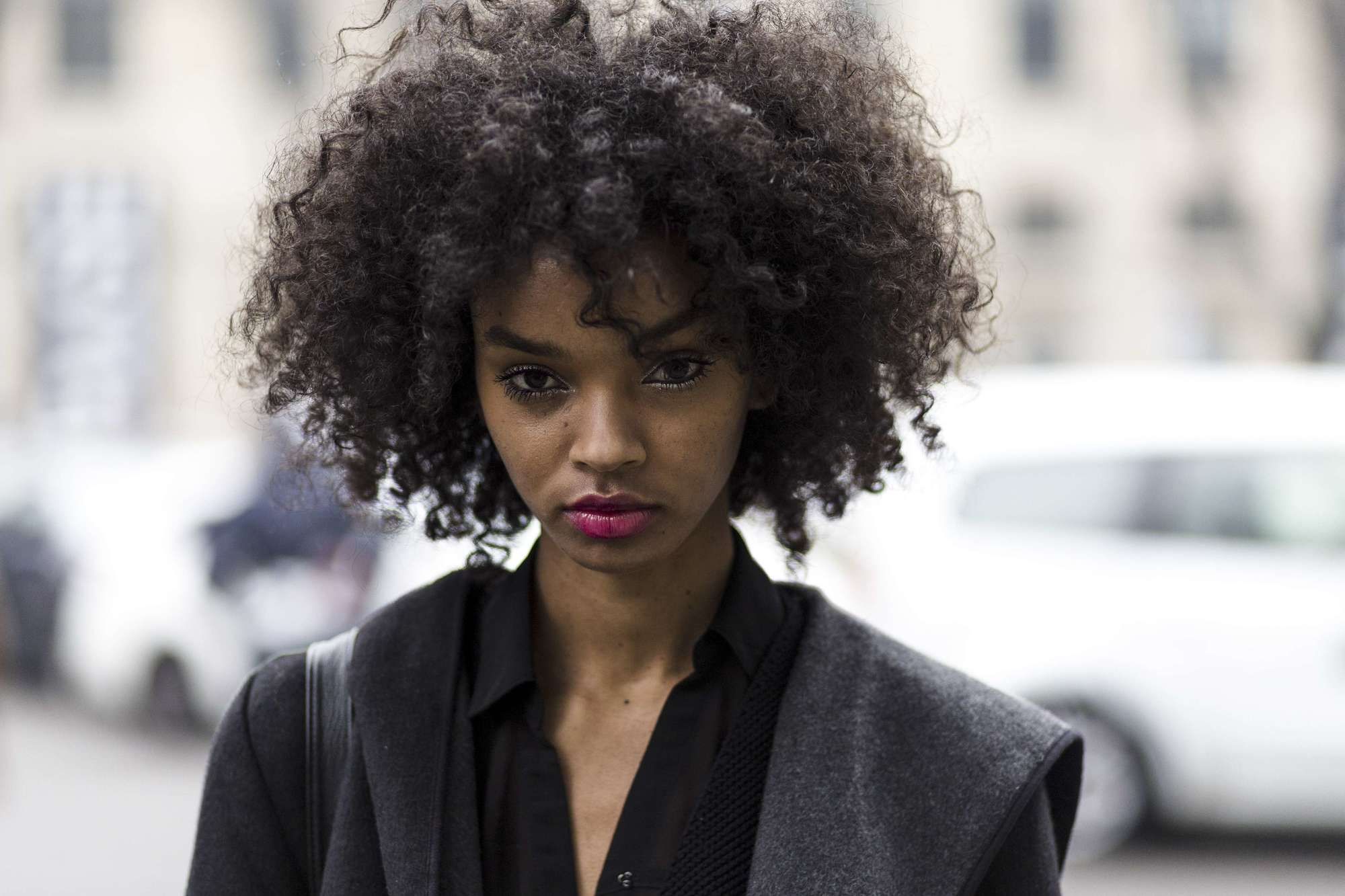 close up street style shot of a model with curly natural hair wearing pink fuchsia lipstick