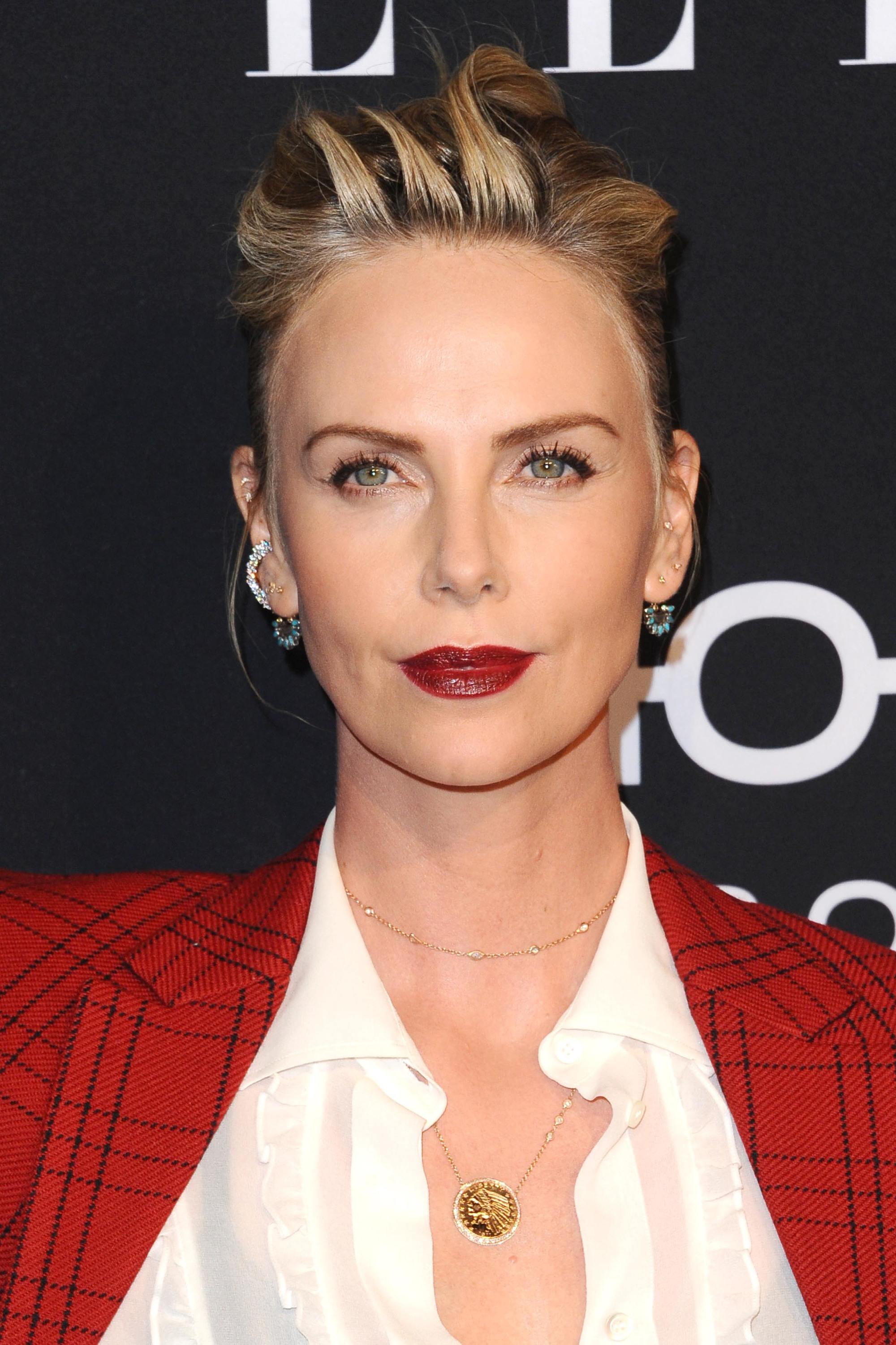 Grown out bangs: Charlize Theron with blonde hair in quiffed back updo wearing a red blazer and white shirt.