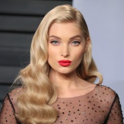 close up shot of Elsa Hosk with champagne blonde hair styled into vintage waves, wearing red lipstick and black dress