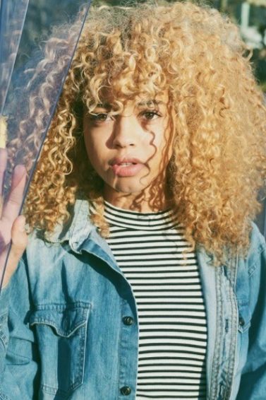 blonde natural haired woman with a full fringe wearing a denim jacket and striped tshirt