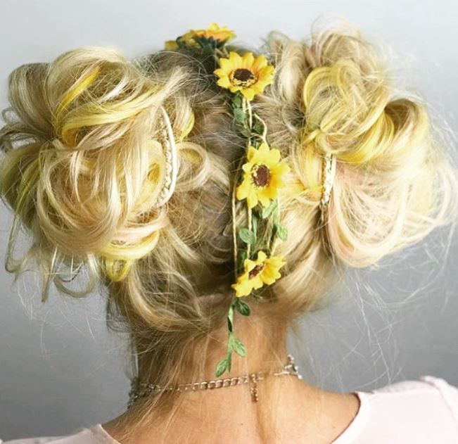 back view of woman with blonde hair in double space buns with sunflowers down the centre parting