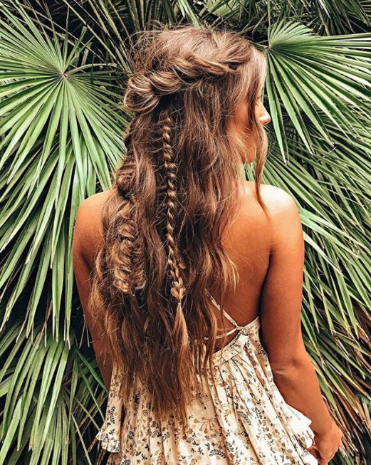back view of woman with long wavy tousled hair in half-up rose twist and braided style standing against palm leaves