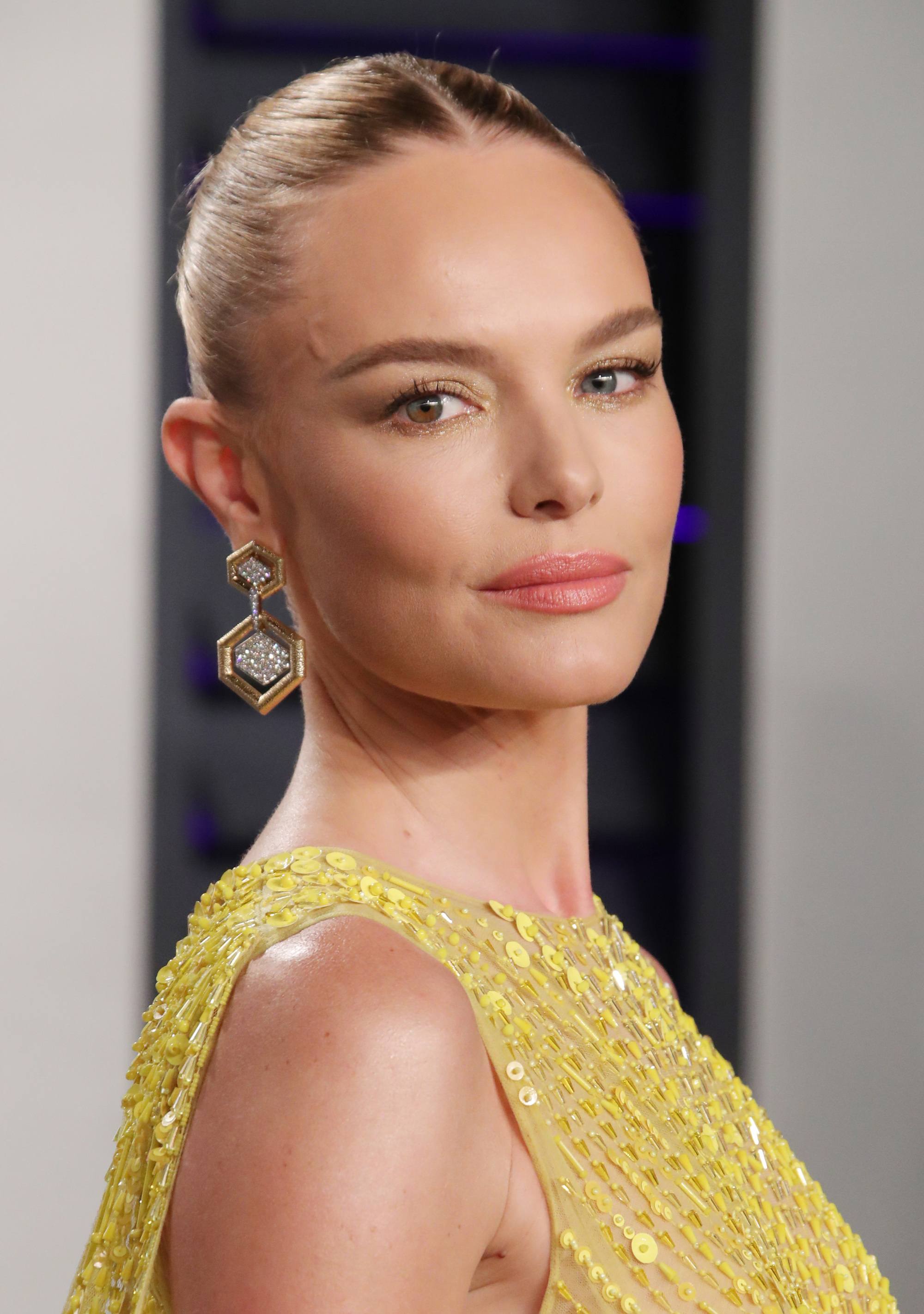 Growing out bangs: Kate Bosworth with straight hair in smooth and sleek bun updo wearing a yellow dress.
