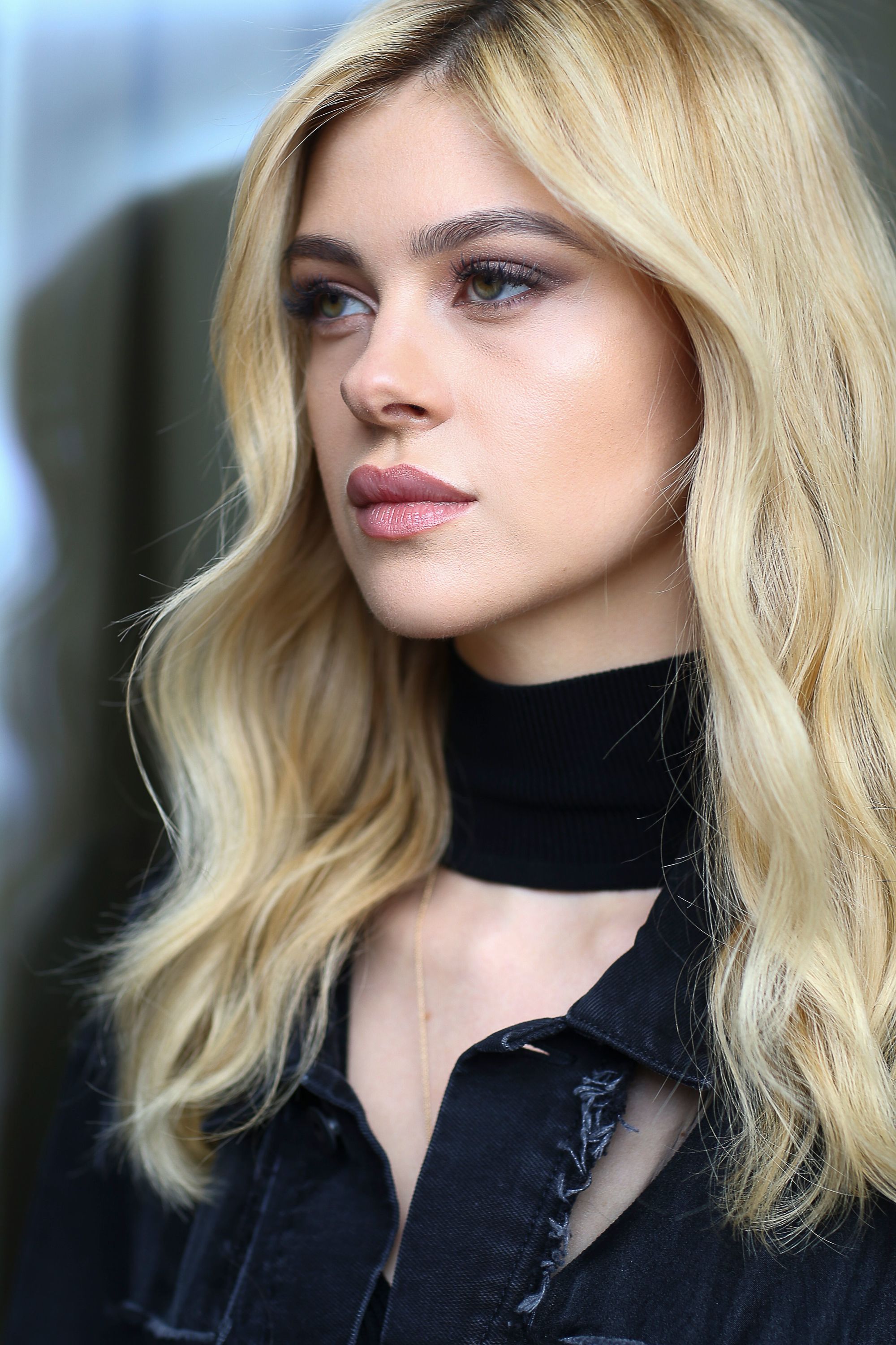 close up shot of nicola anne peltz with wavy sparkly blonde hair, wearing black top and posing