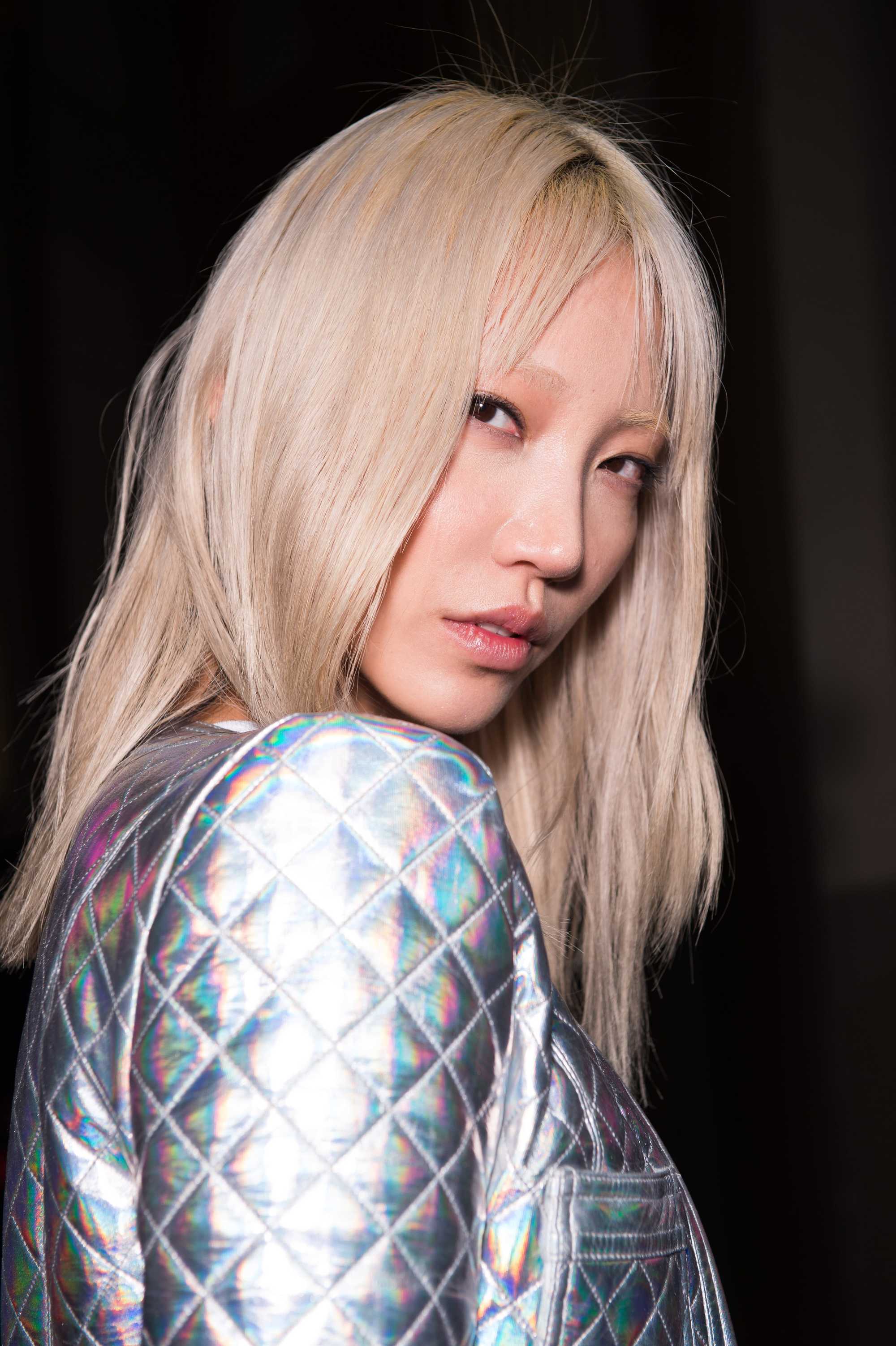 Grown out bangs: Model with platinum blonde hair with bangs parted in the middle, wearing a silver jacket.
