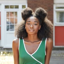 Easy natural hairstyles: Front shot of a model with shoulder-length natural hair styled into half-up space buns, wearing green top and posing outside.