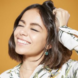 the best dry shampoo guide for oily hair: close up shot model with brunette bob hair scrunching her hair with her hand and wearing a leaf print shirt