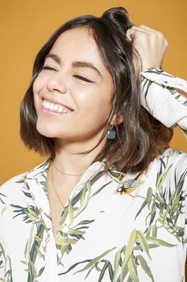 the best dry shampoo guide for oily hair: close up shot model with brunette bob hair scrunching her hair with her hand and wearing a leaf print shirt