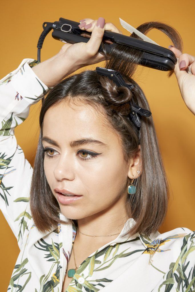 woman with shoulder length dark brown hair using a straightener to style her hair