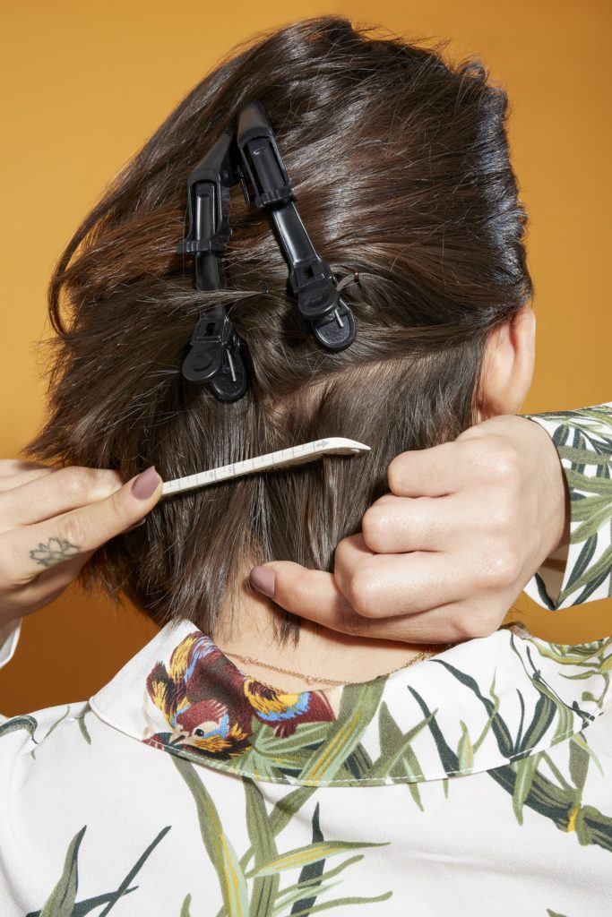 back view of a woman with shoulder length dark brown hair using a comb to section her hair