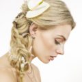 close up shot of model with loose side braided ponytail with flower in it, wearing yellow top and posing outside
