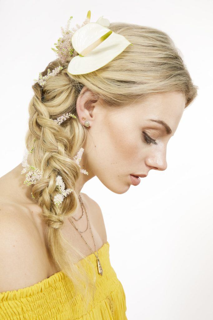 close up shot of model with loose side braided ponytail with flower in it, wearing yellow top and posing outside
