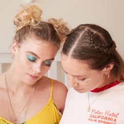 heart braid tutorial: close up shot of two models, one with space buns, the other with a half-up, half-down heart braid, one wearing a white top and the other wearing a yellow sundress