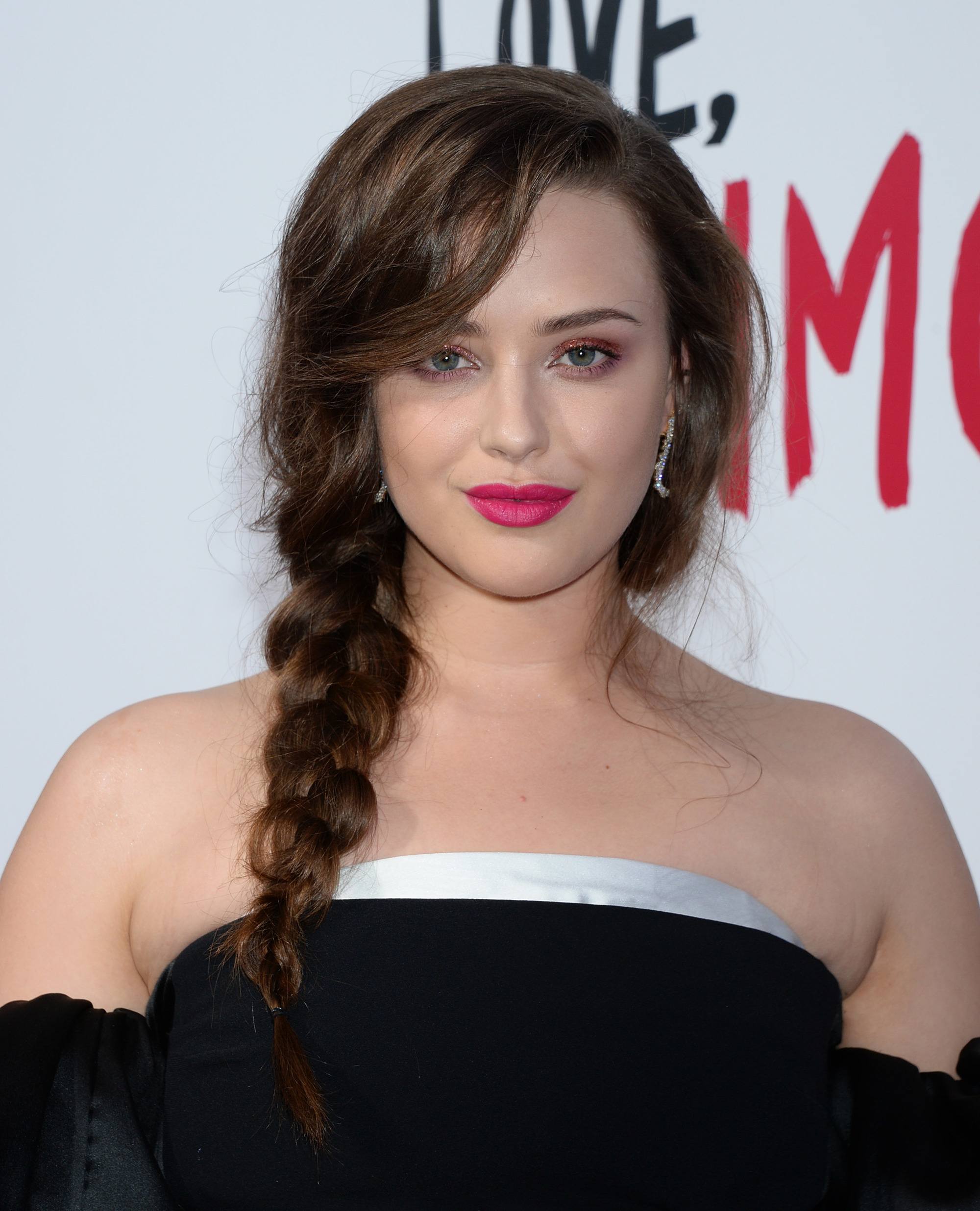 katherine langford with long brown wavy hair styled in a side braid on red carpet event