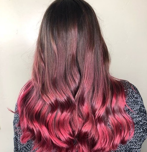 close up shot of woman with neon pink and red violet hair, wearing grey jumper and posing in a hair salon