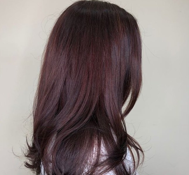 close up shot of woman with sleek, layered long red violet hairstyle, wearing white top and posing in a hair salon