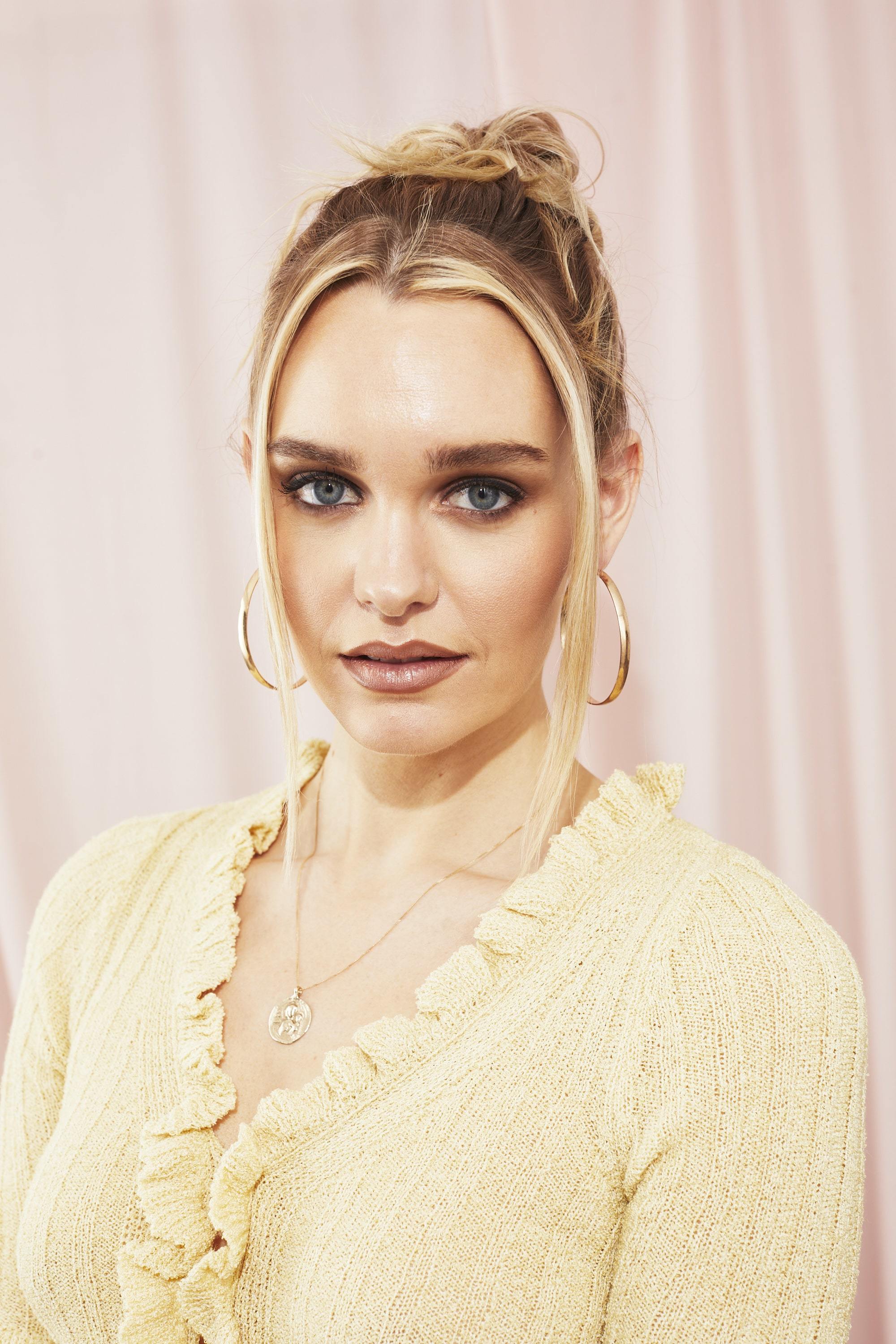 Blonde with her hair in a '90s inspired updo with loose tendrils of hair around her face