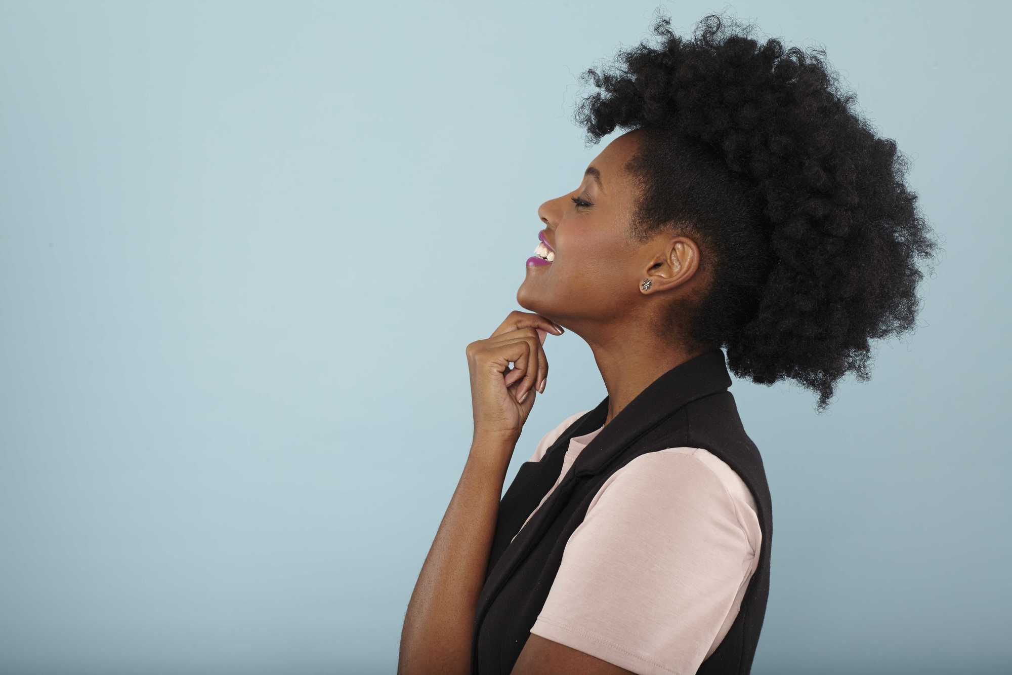 Easy natural hairstyles: Close up shot of model with natural hair frohawk hairstyle, wearing black and white top posing in a studio.