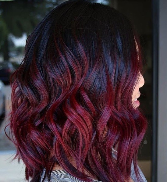 close up shot of woman with a wavy red violet long bob, wearing grey top and posing outside