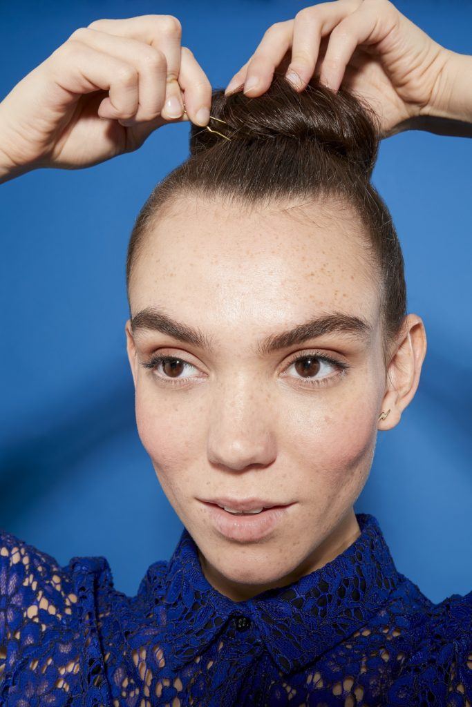 woman with brunette hair in a tight bun pinning it in place, wearing a blue lace outfit