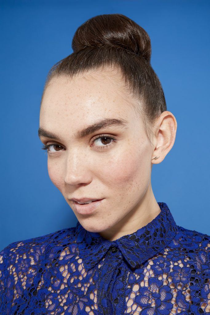 woman with brunette hair in a tight bun, wearing a blue lace outfit