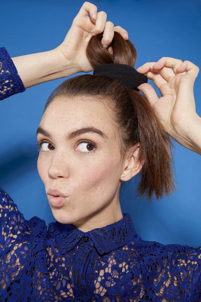 woman with long brunette hair pulling her hair into a ponytail, posing, wearing a blue lace outfit