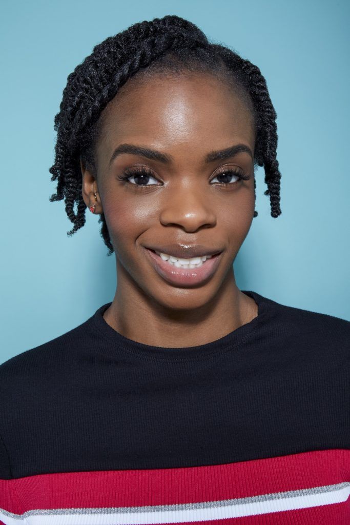 woman with natural black hair styled into small twists, looking at the camera smiling
