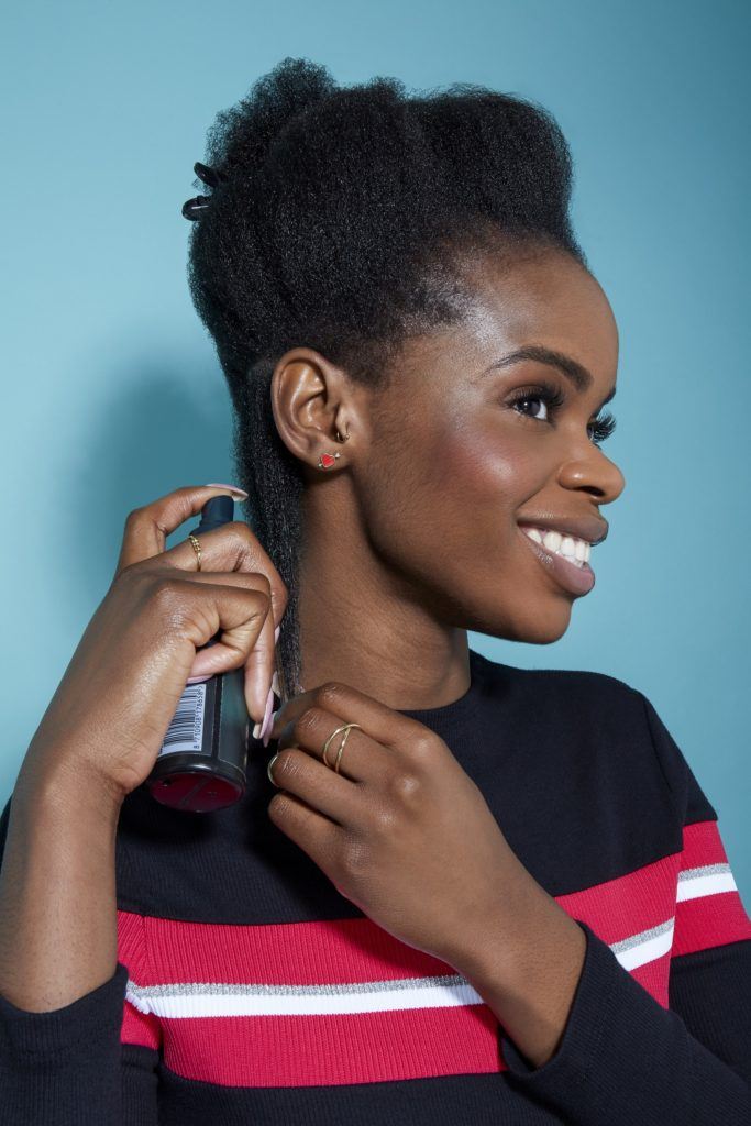 woman with natural black hair spraying a leave in conditioner to her hair