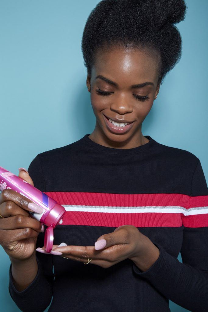 woman with natural black hair looking down applying a hair product into her hands