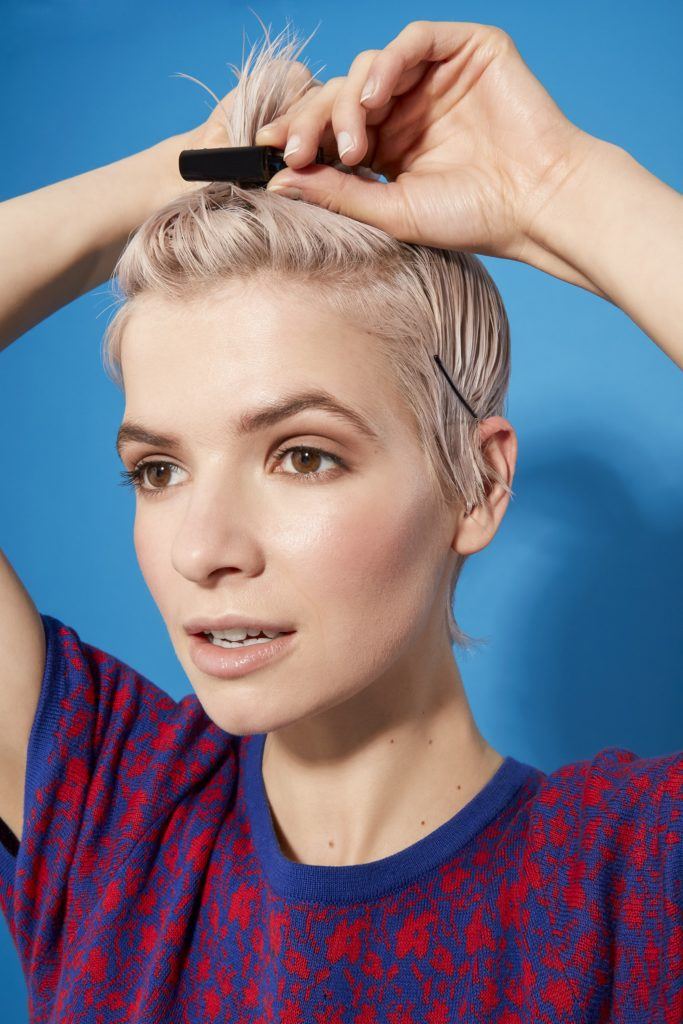 woman with platinum blonde hair in a pixie cut style using pins and clips to section her hair ready for styling